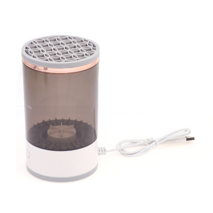 Rechargeable makeup brush cleaner with a gray and rose gold design; features a transparent body and a USB charging cable.