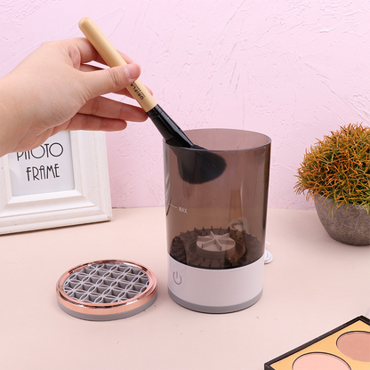 Rechargeable makeup brush cleaner with a transparent chamber. A hand holds a black brush above it.
